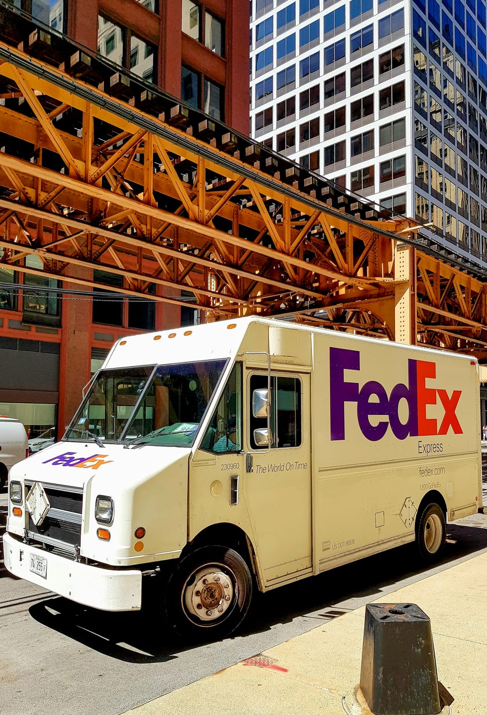 FedEx delivery truck on a city street beneath elevated train tracks